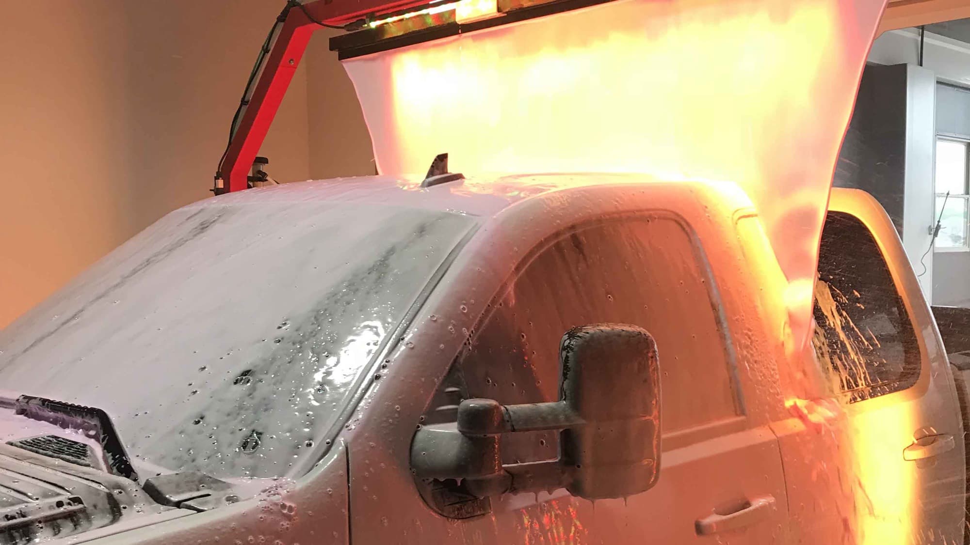 A pickup truck covered in cleaning foam inside a wash bay